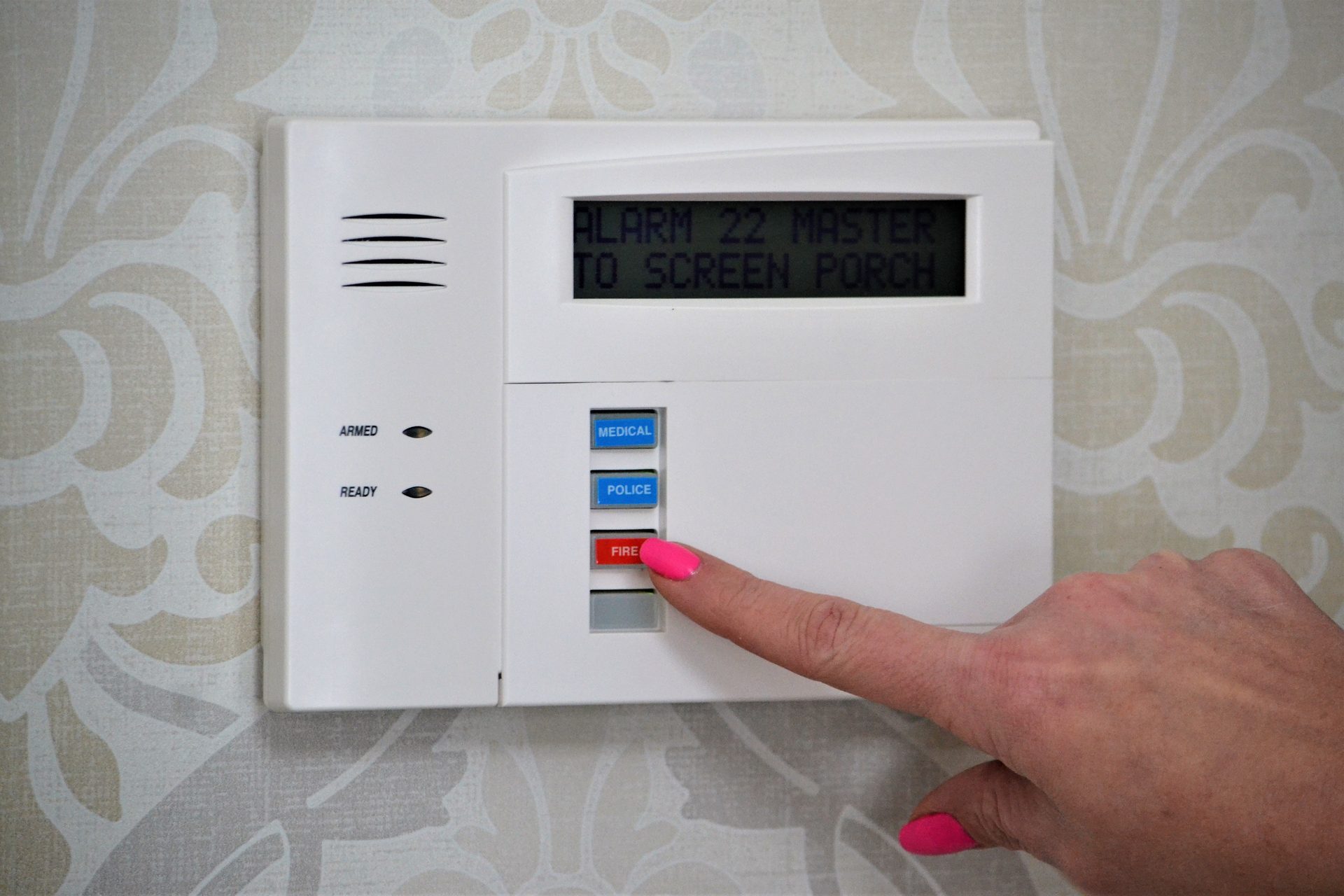 Woman&rsquo;s finger pressing a button on an alarm system keypad with &ldquo;Medical&rdquo;, &ldquo;Police&rdquo;, and &ldquo;Fire&rdquo; buttons.