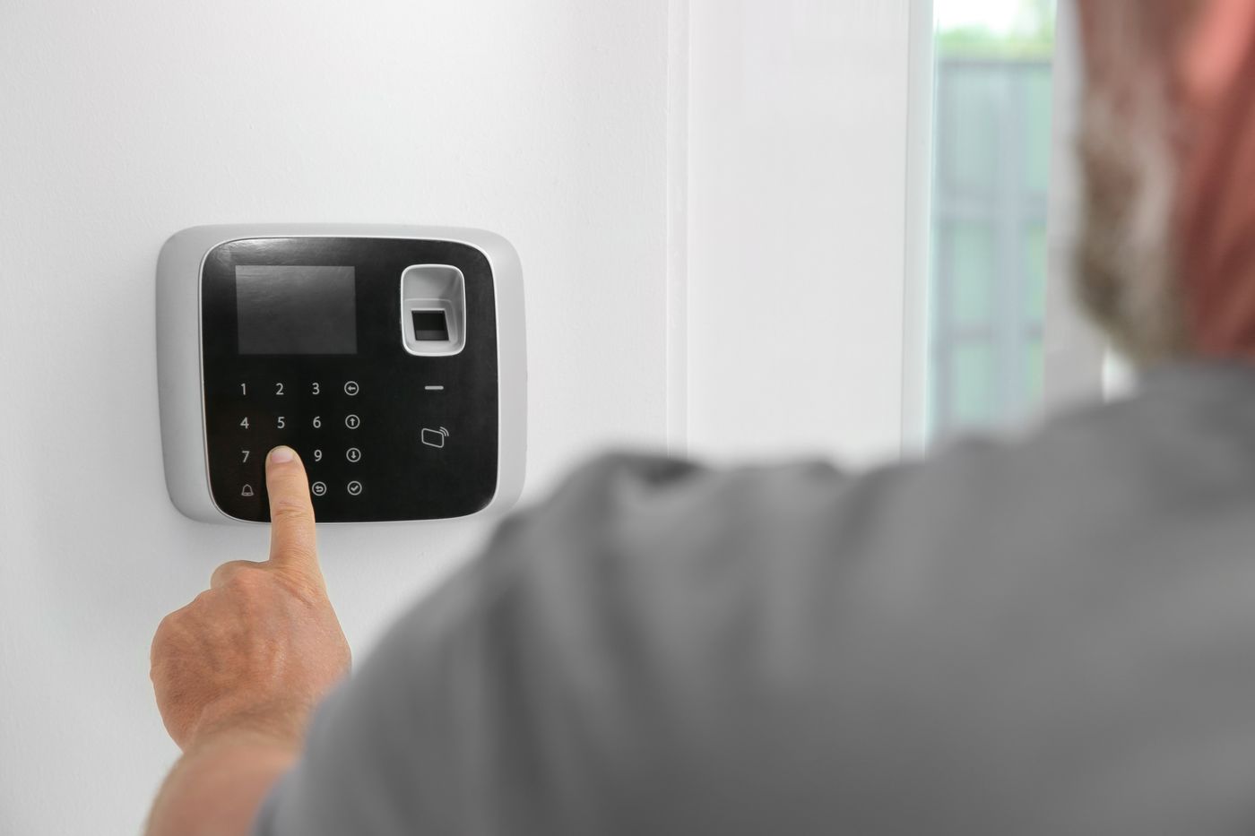 Close-up of a man entering a numeric code on a home security keypad.