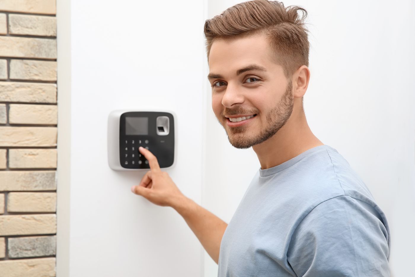 Young man entering security code on alarm system keypad indoors in Delray Beach.